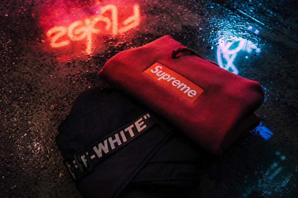 Supreme red box logo and Off-White text logo garments on wet neon-lit concrete
