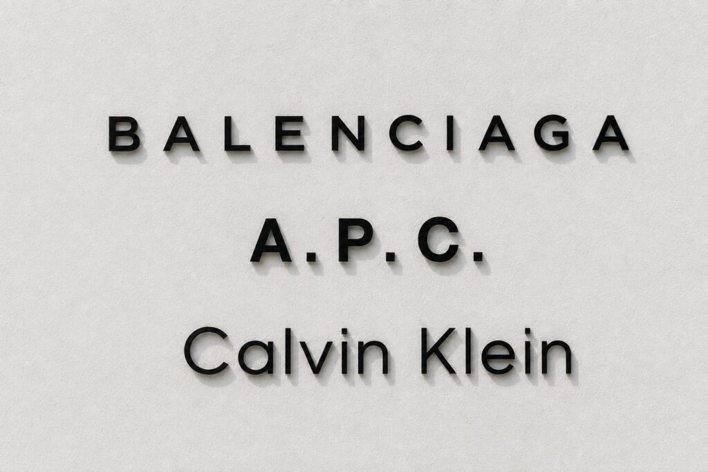 Balenciaga, A.P.C., and Calvin Klein wordmarks arranged vertically on white plaster wall